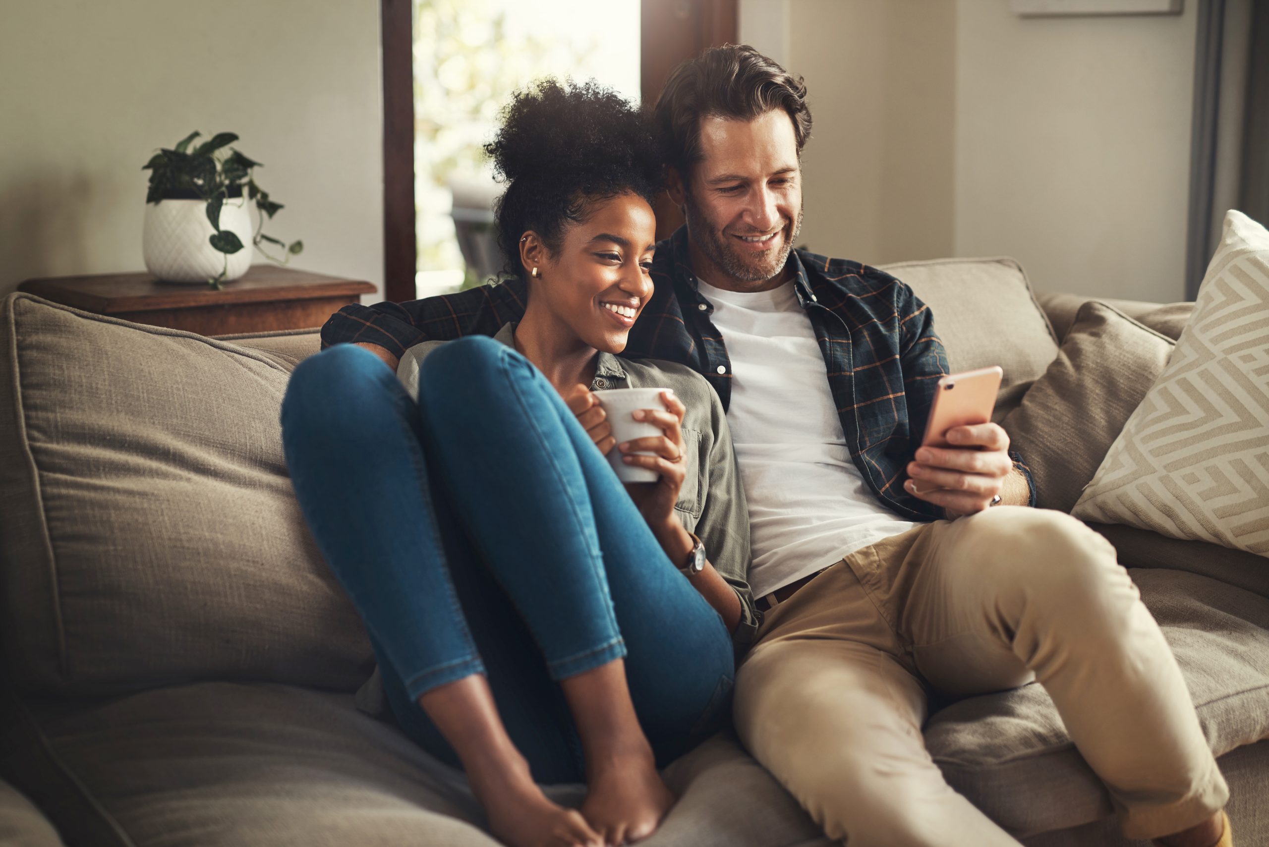 Happy couple sat together on sofa scrolling through phone